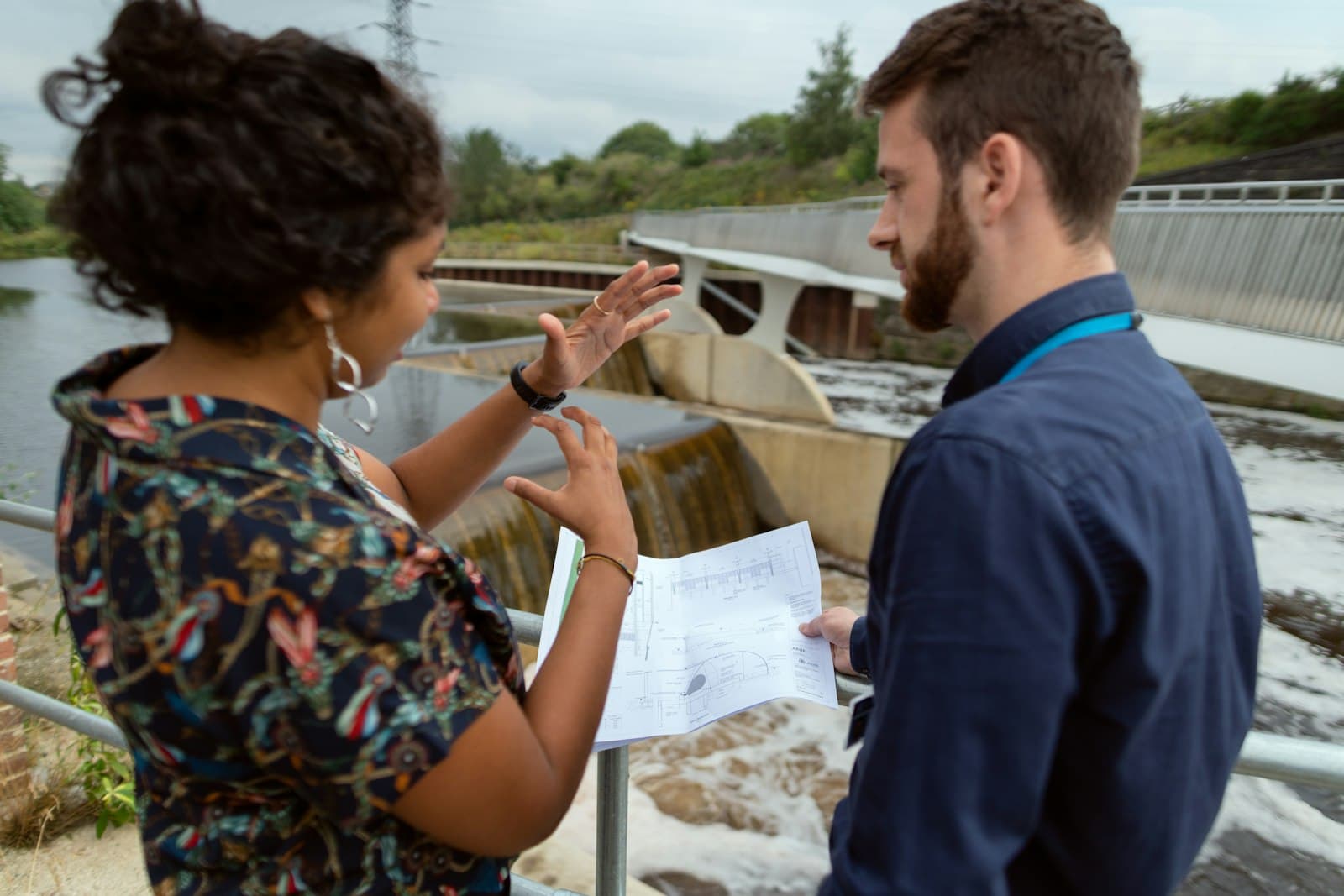 Dos ingenieros revisan un plano técnico junto a una estructura hidráulica de un río