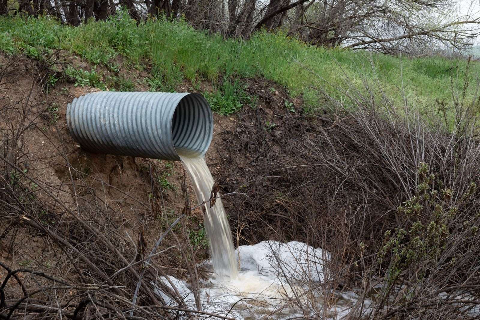 Tubería metálica corrugada que descarga agua en una quebrada rodeada de vegetación